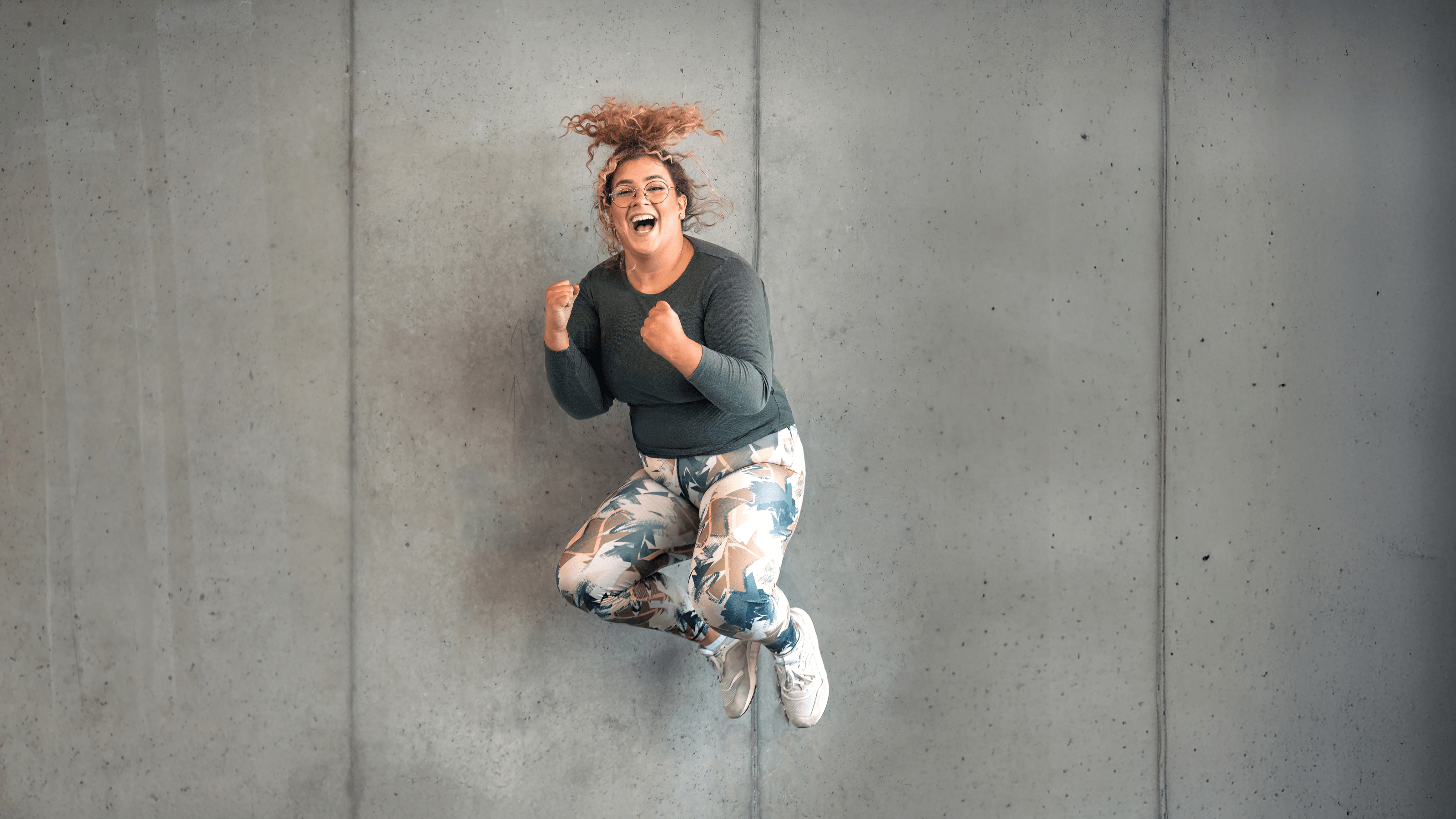 Ein INJOY Fitnessstudio-Mitglied springt vor Glück in die Luft und lacht dabei in die Kamera.