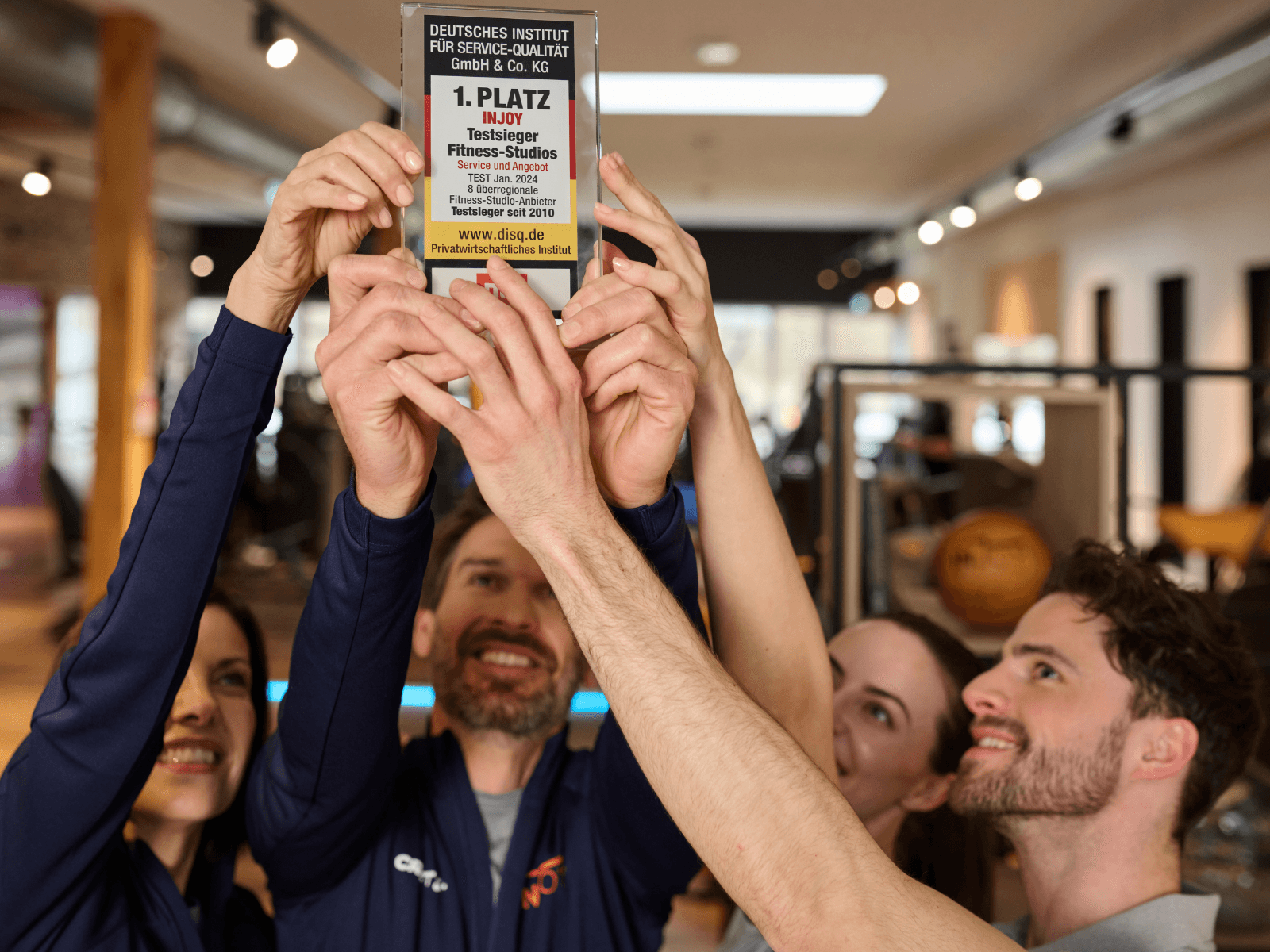 Eine Gruppe von INJOY Trainern und Trainerinnen heben den Testsieger Award in die Höhe.